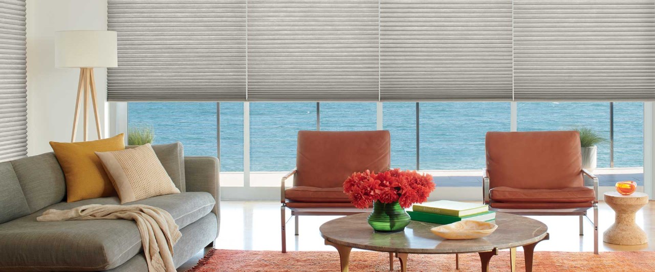 Grey couch and two red chairs overlooking ocean with Duette shades.