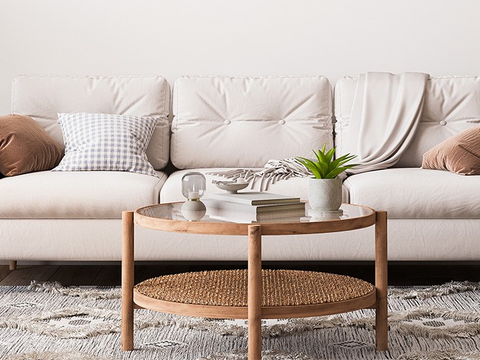White upholstered couch with brown decorative cushions and round rattan and glass top coffee table.